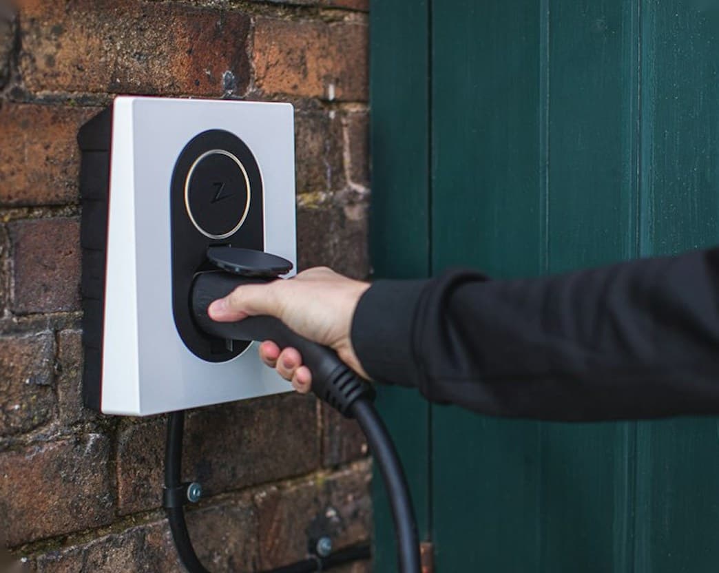 Hand plugging a cable into a wall-mounted EV charger