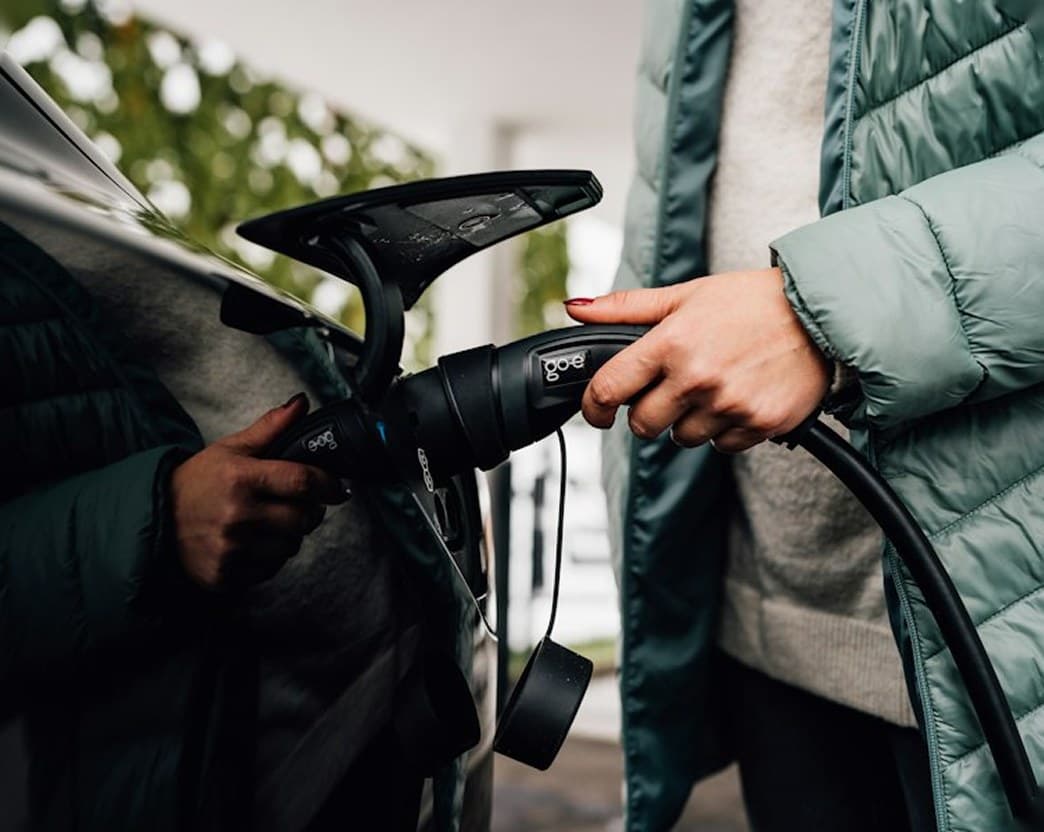 Person holding an EV charging connector next to a car